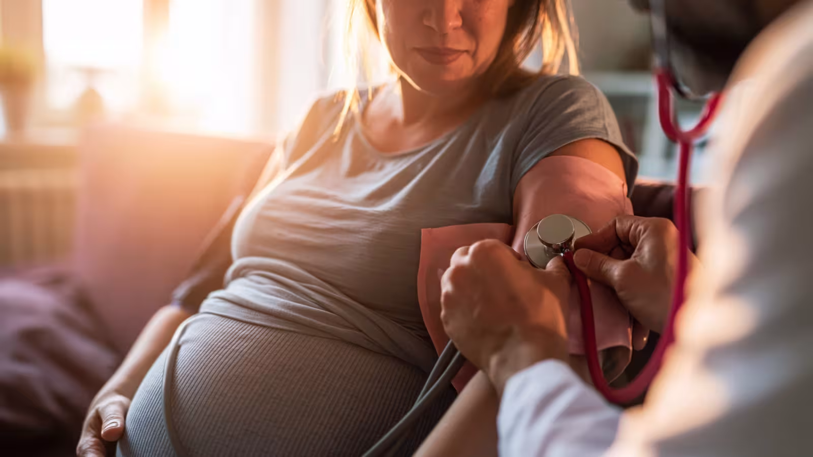 A clinician examining a pregnant woman with a stethoscope during an antenatal appointment.