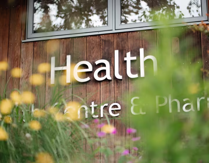 The Health Centre and Pharmacy sign on the wooden frontage, framed by wildflowers
