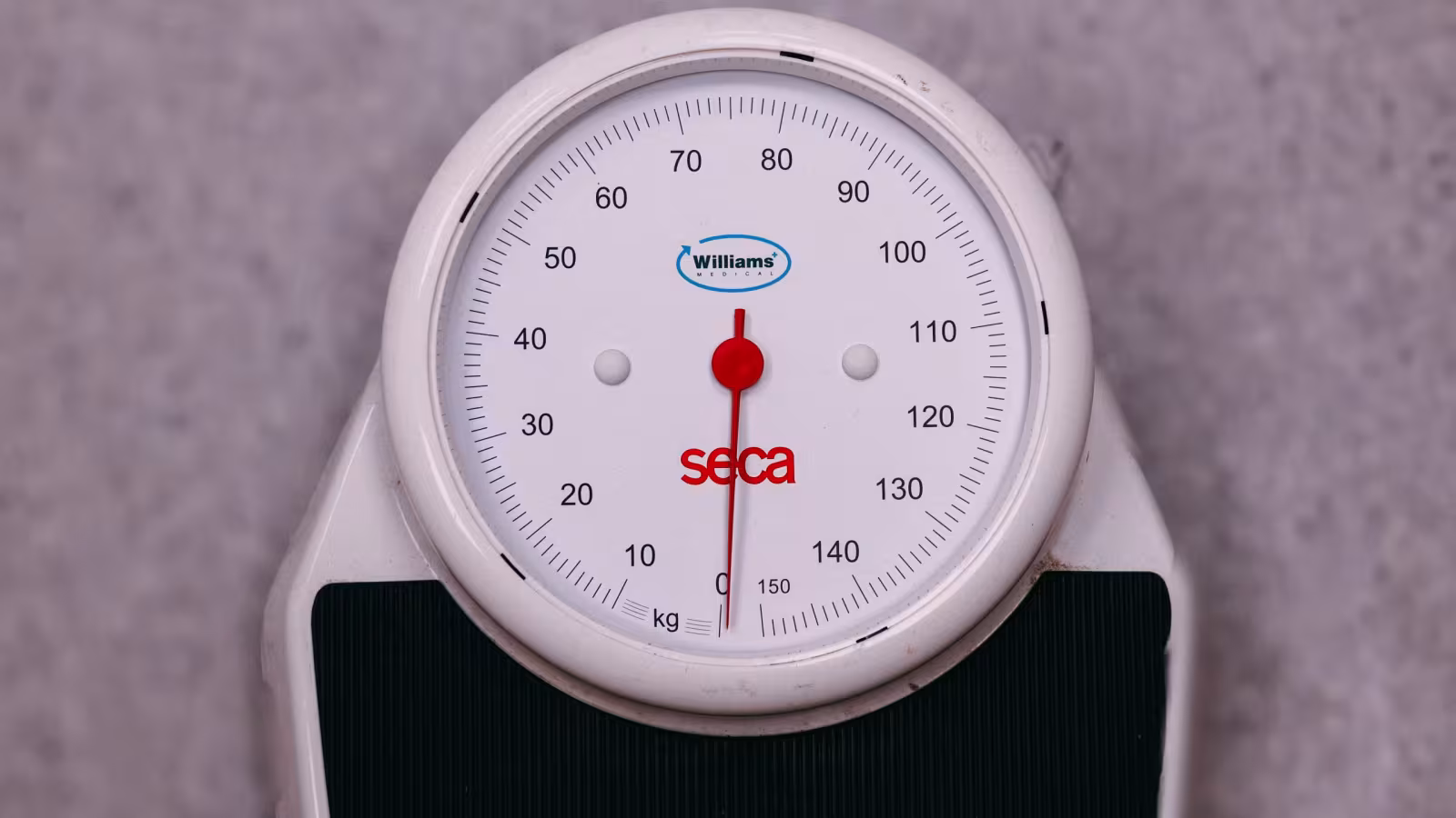 The dial of a consulting room weighing scale, its needle resting at zero.